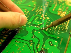 View the event “Soldering course”; image description: A hand holding a piece of soldering tin against the tip of a soldering iron, on a green circuit board