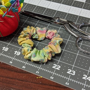 Vis arrangementet «Sykurs - Lag en scrunchie»; bildebeskrivelse: En hårstrikk, en stoffsaks og en nålpute